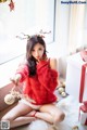 A woman in a red sweater sitting on the floor next to a Christmas tree.