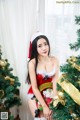 A woman in a santa claus outfit posing next to a Christmas tree.